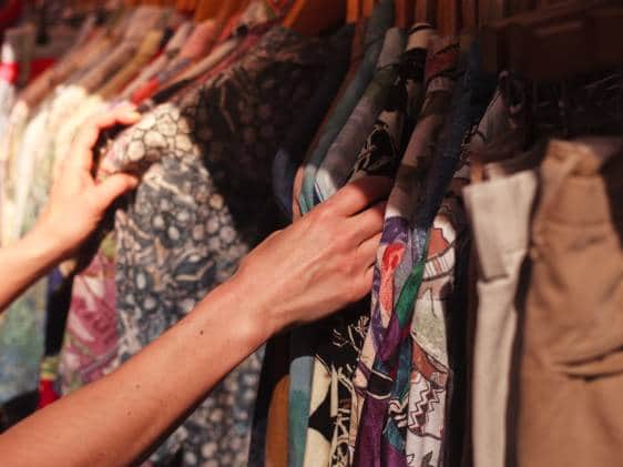 A young woman is browsing a rail of clothes at a street market